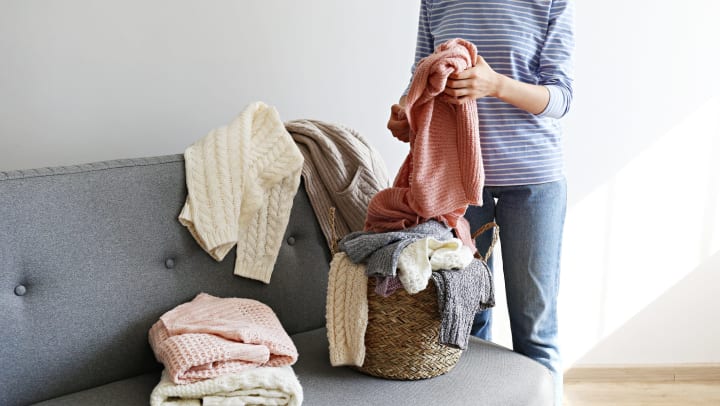 A woman folding up winter sweaters on her couch