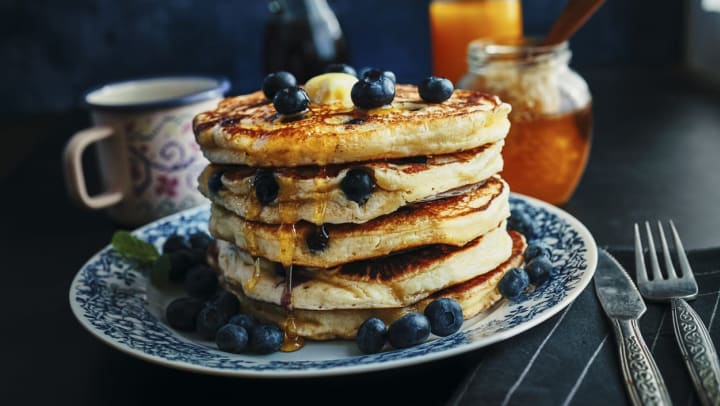 Stack of fluffy pancakes with maple syrup and fresh blueberries sitting on a blue patterned plate | breakfast restaurants around destin