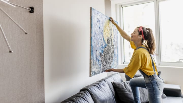  A woman hanging a painting on the wall of her apartment