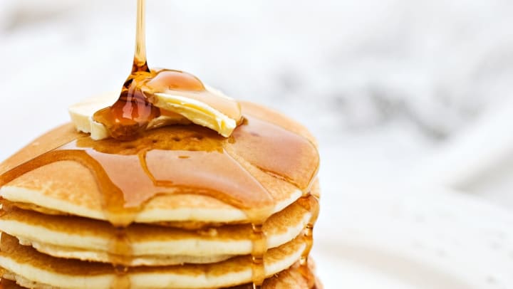 A close-up of maple syrup pouring onto a stack of fluffy pancakes with butter | breakfast places in Albuquerque