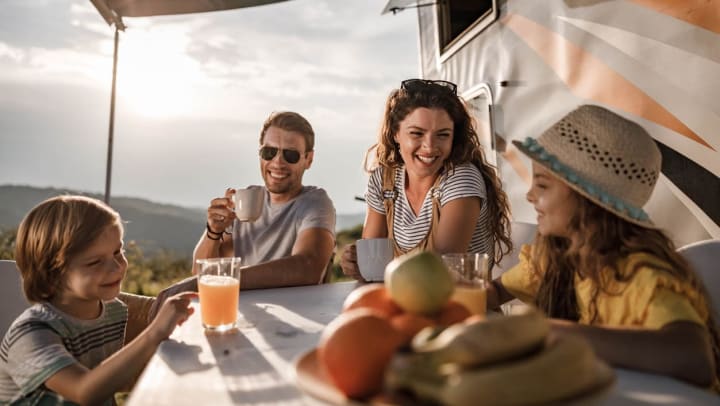 Parents and their children sit outside their RV while camping
