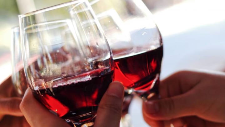 Close-up of three hands holding glasses of red wine while making a toast. 