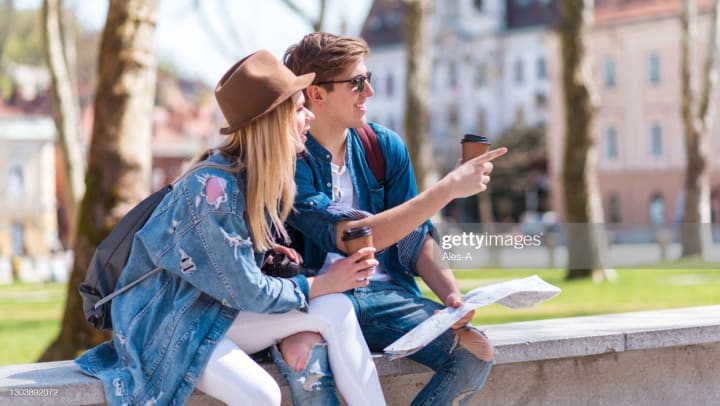 Young man and woman sitting on a brick wall and looking at something off camera.