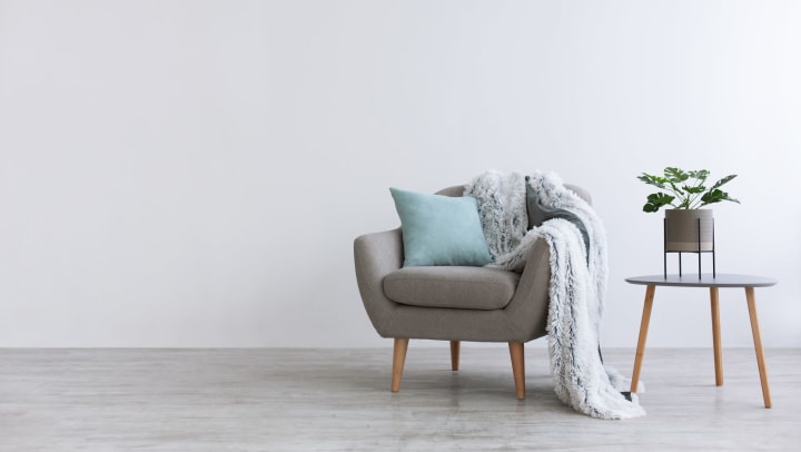 Gray chair with a light blue pillow and a faux throw blanket draped across it.