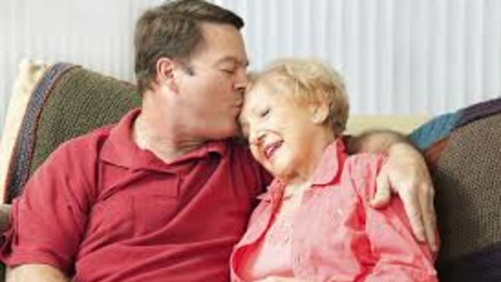 A man kissing his elderly mother on the forehead. 