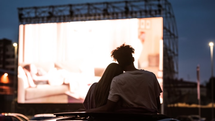 Silhouetted view of a couple embracing while watching a movie in a drive-in.