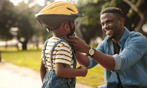 Dad putting a bike helmet on his son at Bancroft Towers in San Leandro, California