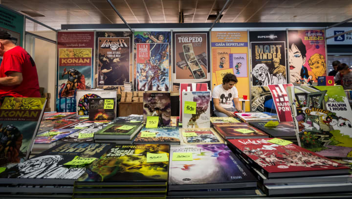  a man wearing a Mickey Mouse shirt looks through comics among a large collection | Albuquerque