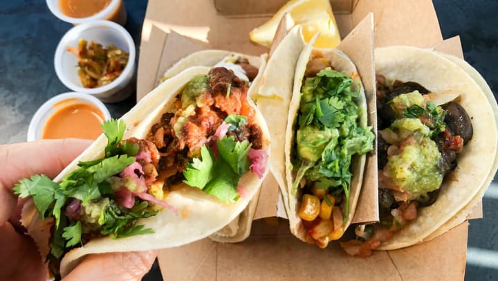 a person holding a taco over a takeout container of tacos and sauces| taco shops in Nashville