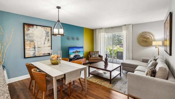 An open apartment living space featuring a dining table with chairs, a sectional couch, and colorful accent walls.