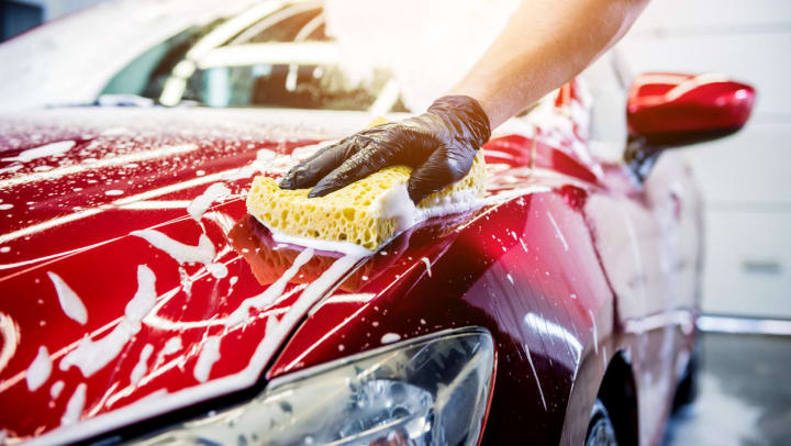 A close-up of a person washing a red car at a Willow Park car wash.