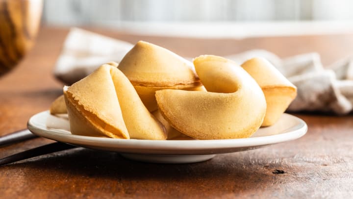 A plate of fortune cookies on a white plate on a table with chopsticks next to them. 