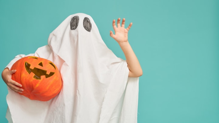 Child dressed as a ghost holding a pumpkin celebrating Halloween at Sedona Ranch