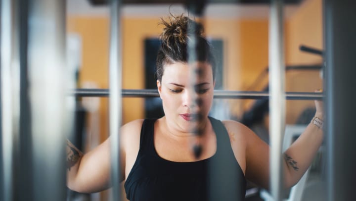 Focused young woman in black athletic wear with a barbell over her shoulders preparing for a back squat at an indoor gym
