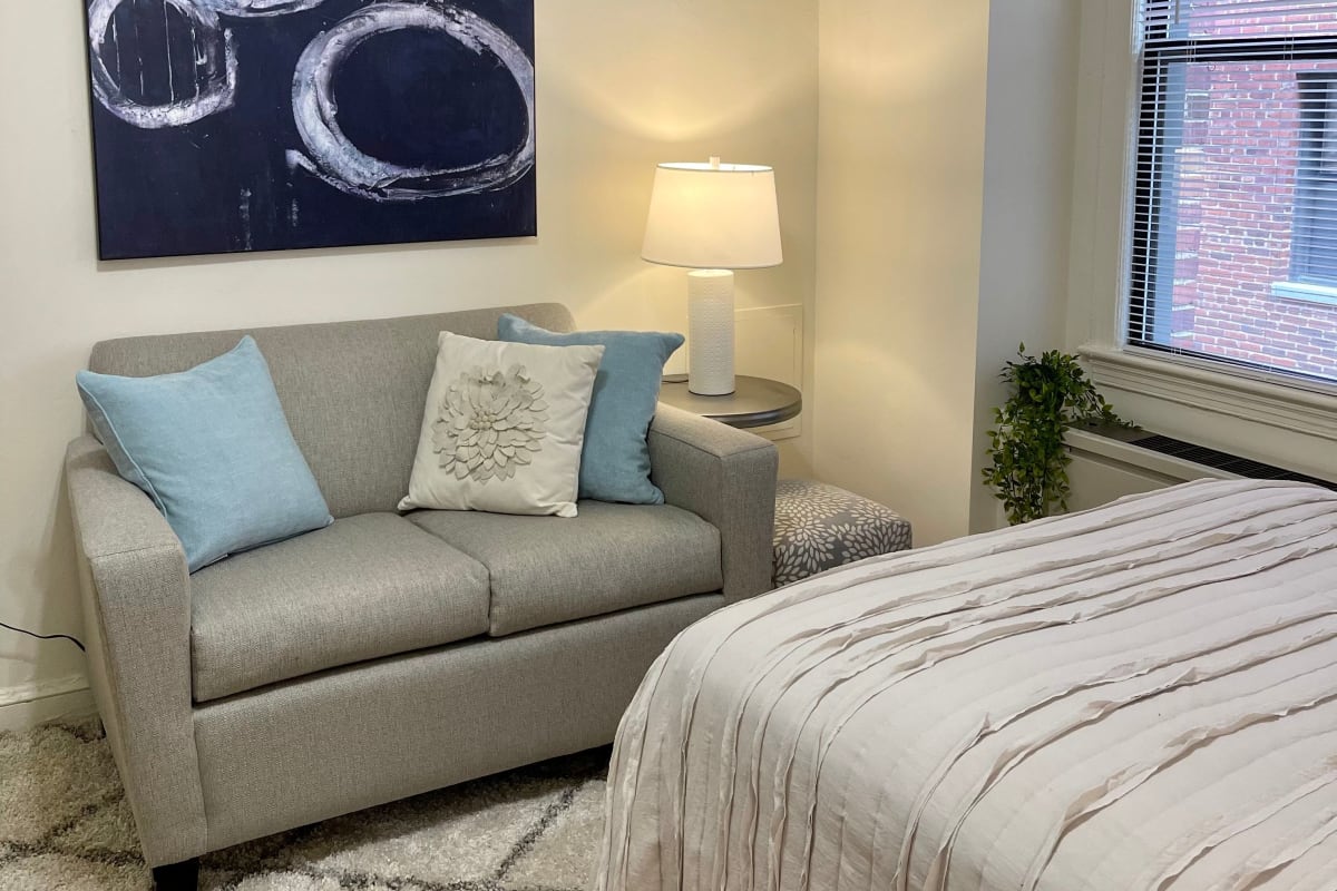 Cozy couch in front of the bed in a model studio home at The Shoremeade Apartments in Washington, District of Columbia