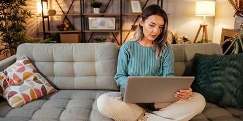 A resident sitting on the couch and working on her laptop in a modern living room at Kernwood Terrace in Los Angeles, California