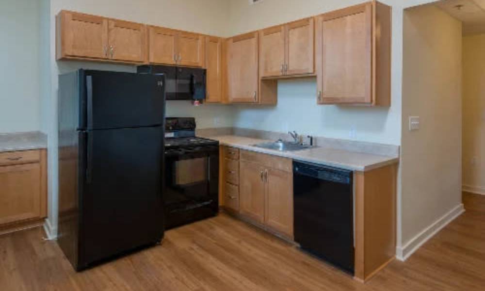 Apartment kitchen with wood cabinets and black appliances at A.L. Miller Village in Macon, Georgia