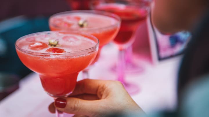 Disembodied hand grabbing the stem of a margarita glass filled with pink liquid. 