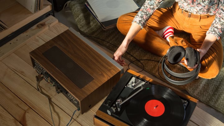Woman listening to music on a HiFi system with turntable, amplifier, headphones, and lp vinyl 