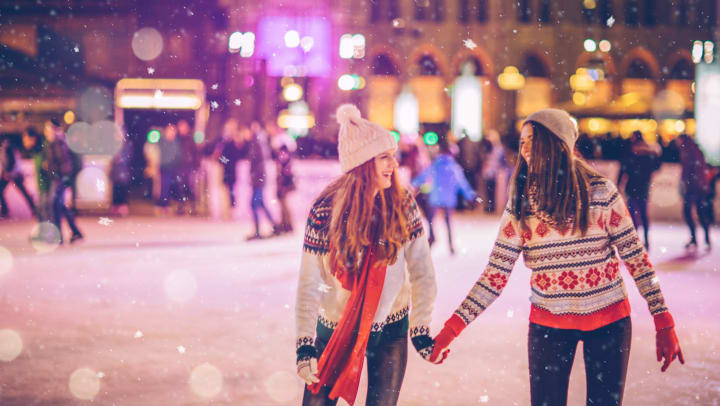 Two women holding hands while skating at an outside skate rink. 