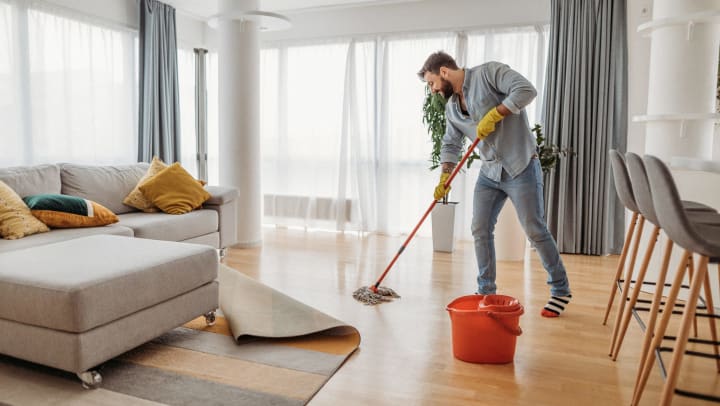 Young man mopping the floor of his apartment.