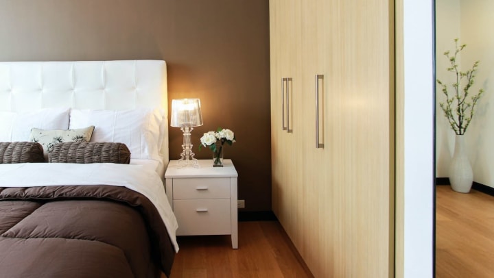 bedroom with brown comforter, white headboard, and a white nightstand with flowers
