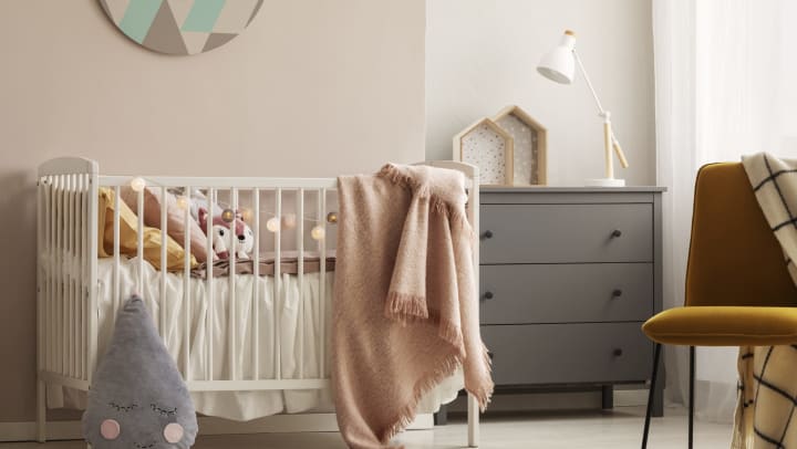 A room with a baby crib, dresser and chair.