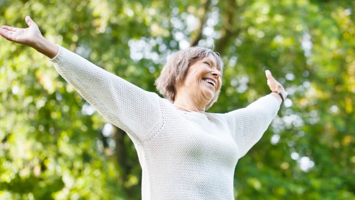 woman outside smiling with arms spread out in joy