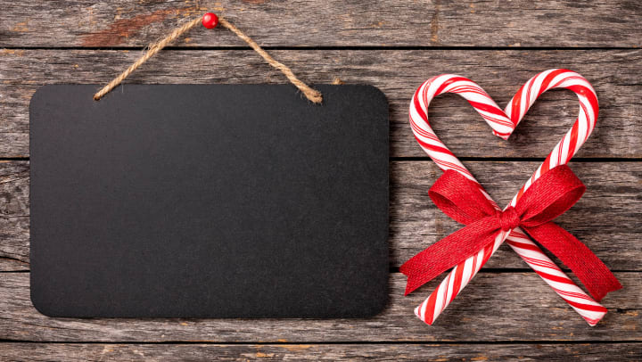 Blank chalkboard sign with candy canes tied with a ribbon in the shape of a heart.