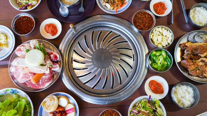 Round table-top barbecue grill surrounded by dishes with a variety of Korean foods