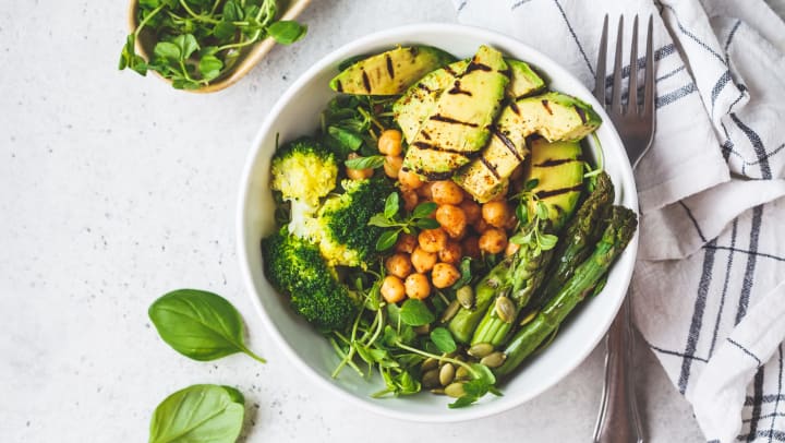 Filled ceramic bowl with grilled avocado, asparagus, chickpeas, pea sprouts, and broccoli.