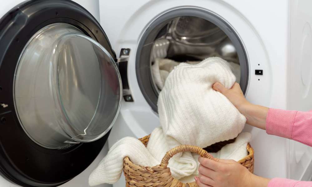 Person placing white towels into a washing machine at Prince Frederick Villas in Prince Frederick, Maryland