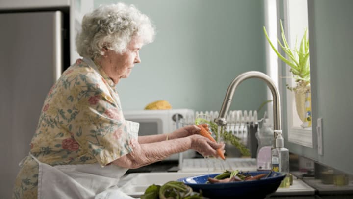 Senior woman with white curly hair cleaning vegetables at a kitchen sink