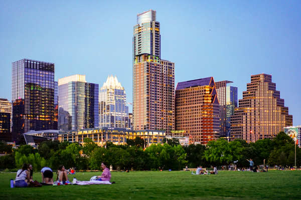 Residents relax on a grassy field at sunset with a city skyline in the background at Mosaic at Mueller in Austin, Texas