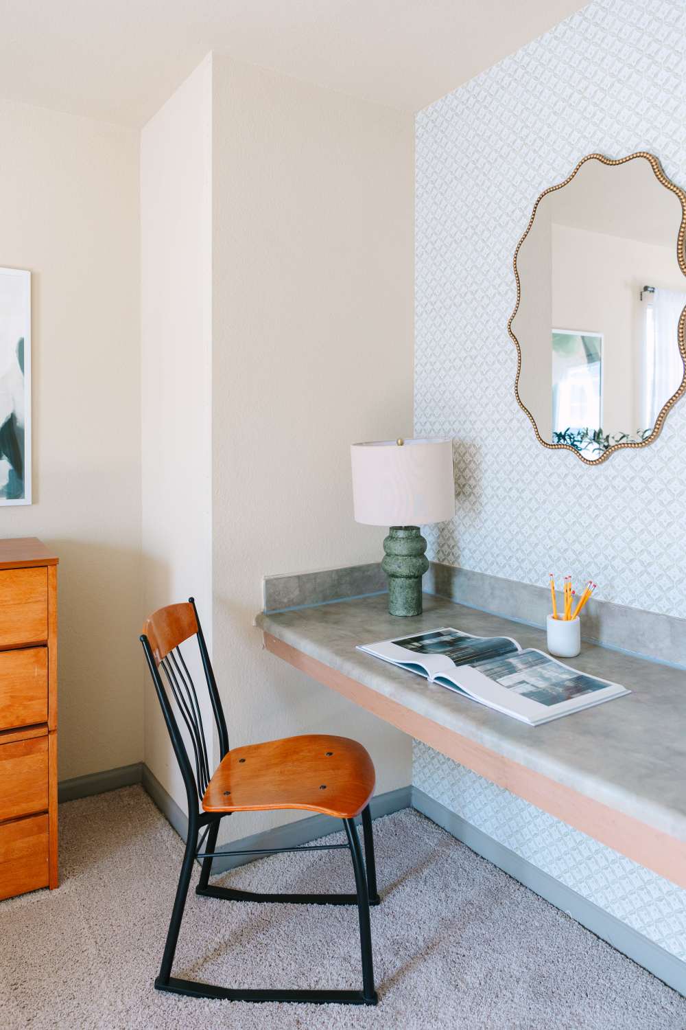 Compact workspace with wood chair, desk, lamp, and wall mirror above counter at The Holly in Lubbock, Texas