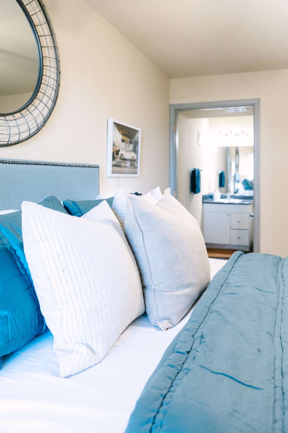 Bedroom with upholstered headboard, layered pillows, and view into ensuite bathroom at The Holly in Lubbock, Texas