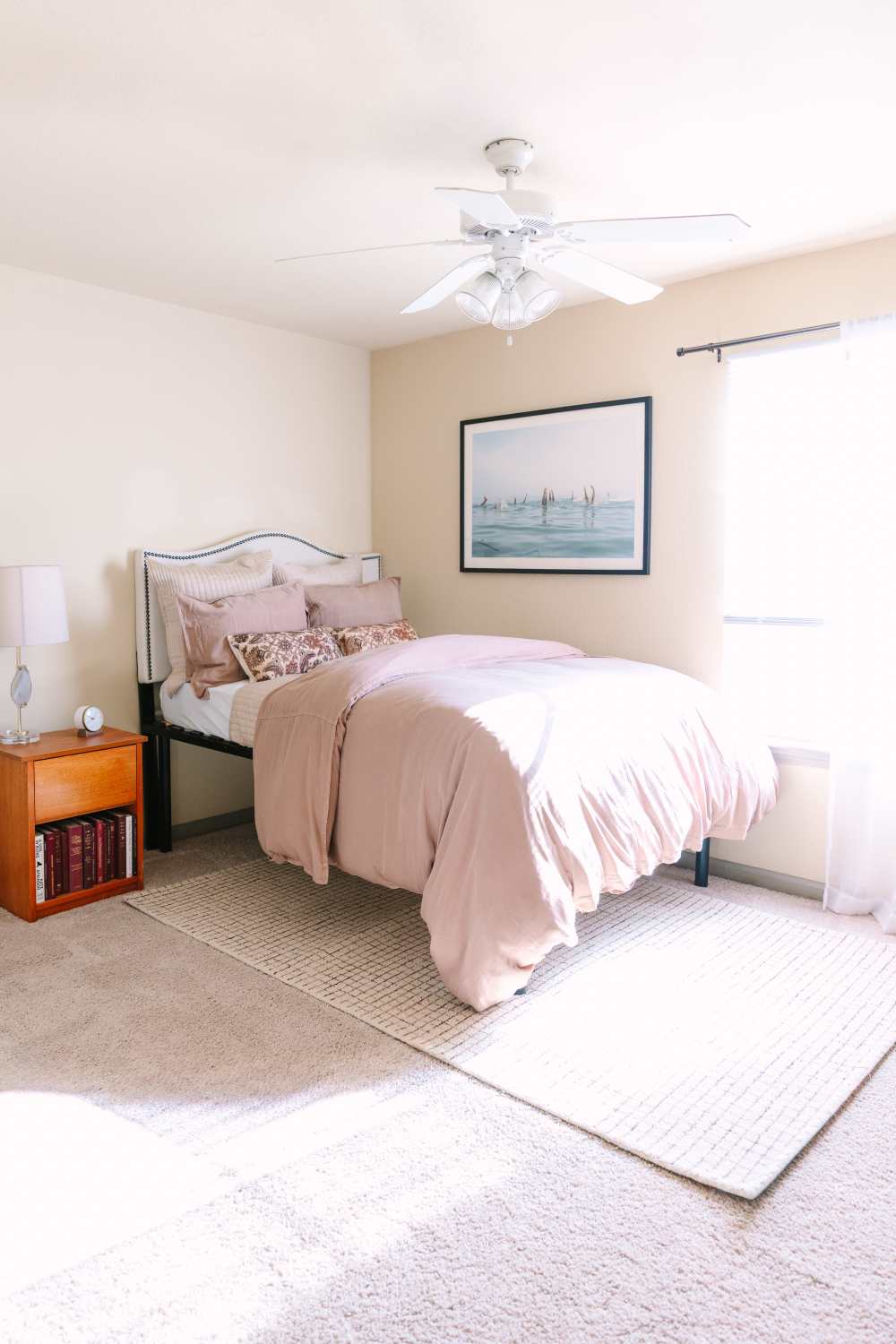 Bright bedroom with bed, nightstand, ceiling fan, and large window with natural light at The Holly in Lubbock, Texas