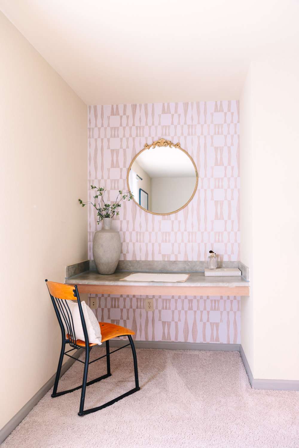 Cozy workspace nook with chair, desk, vase with flowers, and round wall mirror at The Holly in Lubbock, Texas
