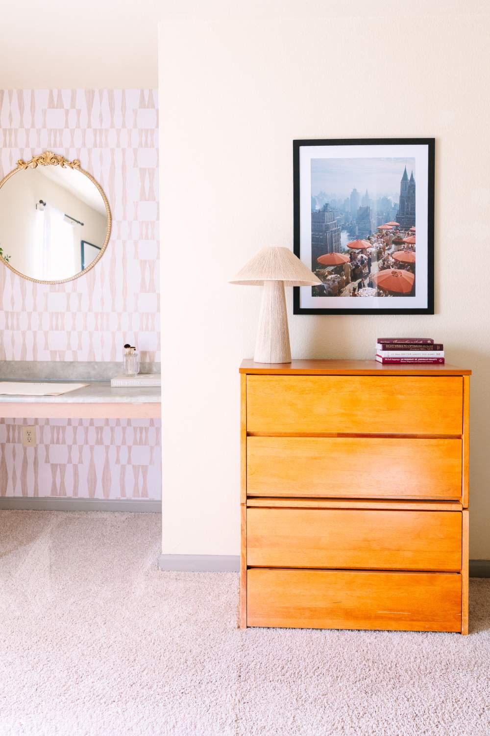 Bedroom with wood dresser, table lamp, wall art, and vanity area with round mirror at The Holly in Lubbock, Texas