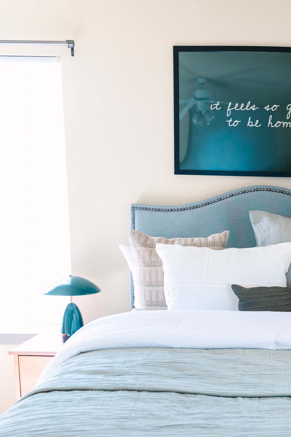 Bedroom with upholstered headboard, pillows, bedside table, lamp, and wall art at The Holly in Lubbock, Texas