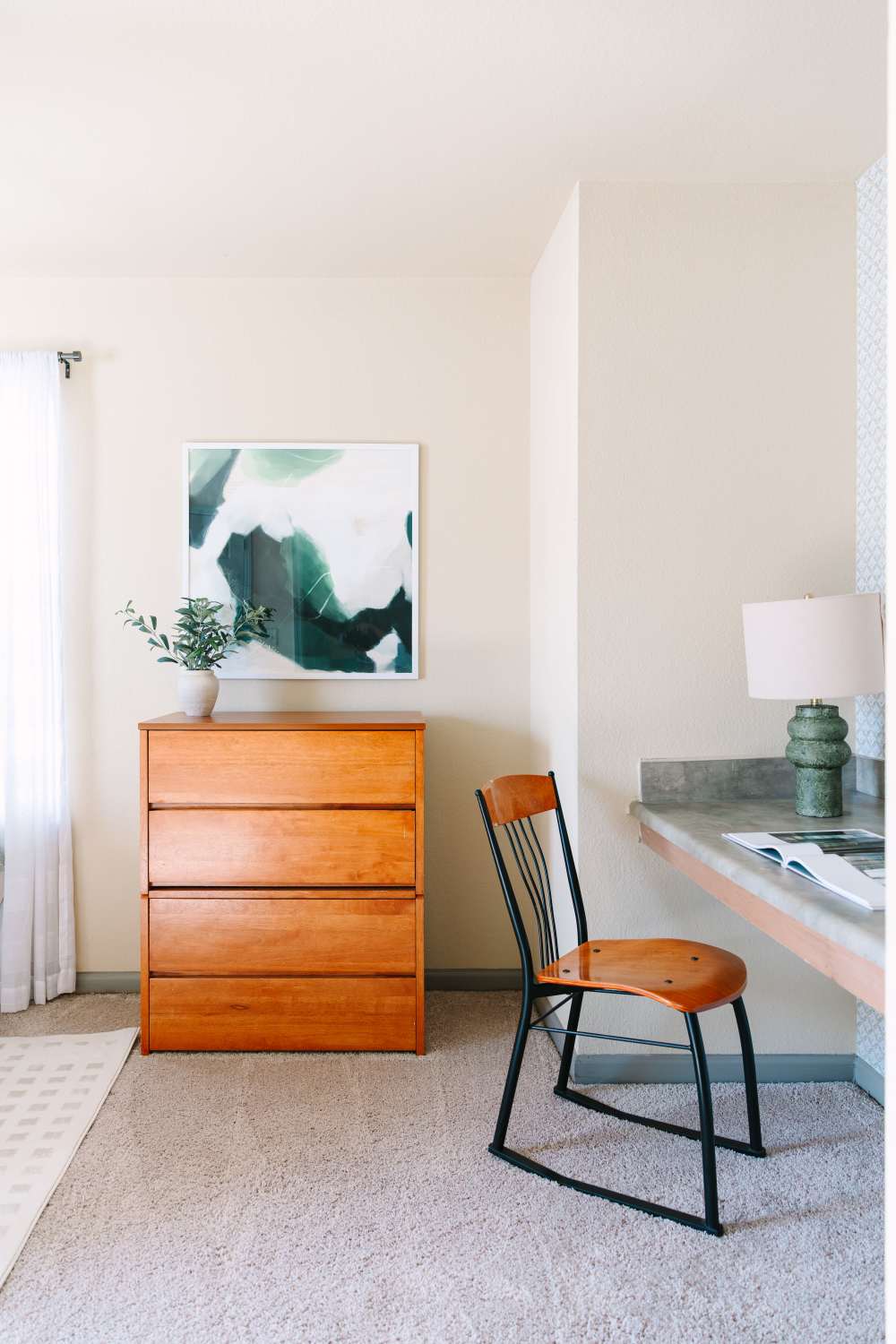 Bedroom with wood dresser, framed wall art, and workspace desk with chair and lamp at The Holly in Lubbock, Texas