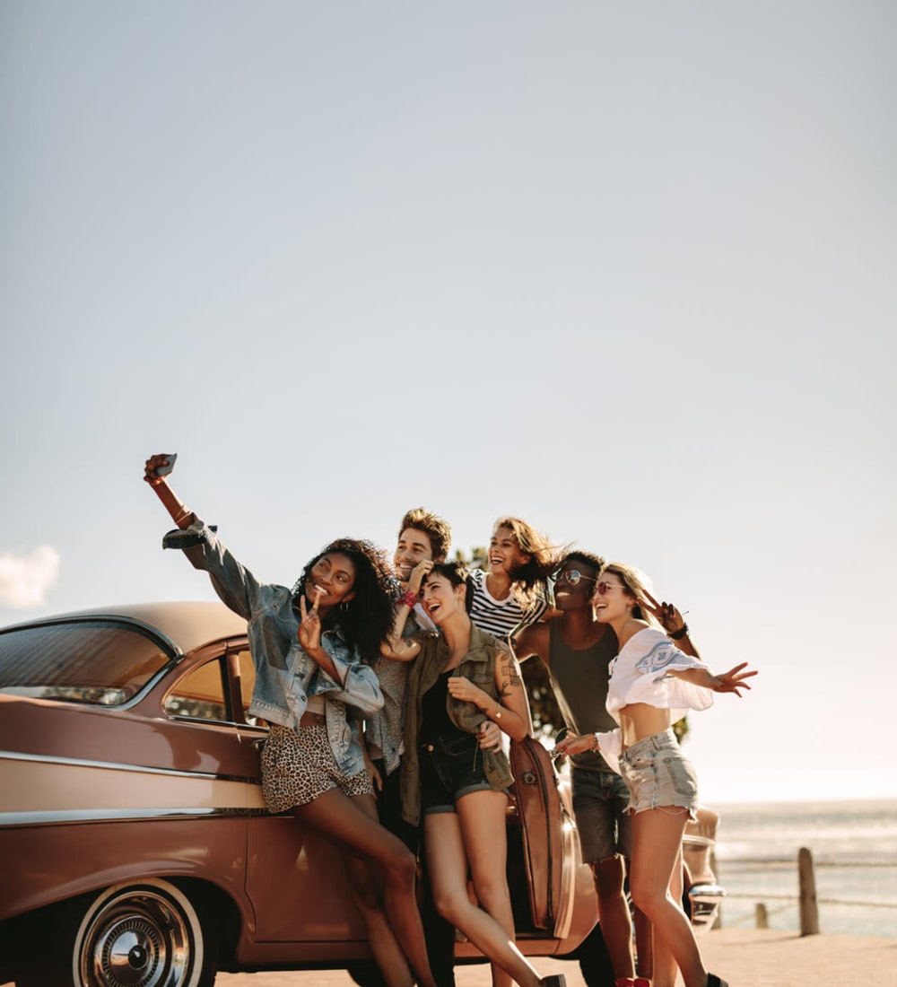 Friends pose for selfie in front of classic car on beach near Campus Quarters in Corpus Christi, Texas