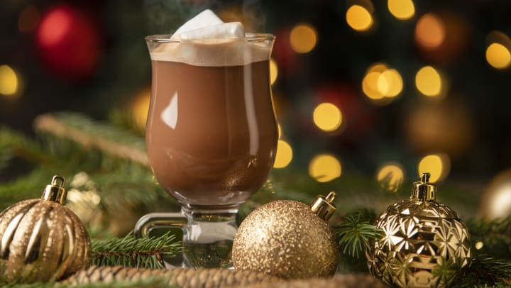 A glass mug of hot chocolate surrounded by ornaments and decorations