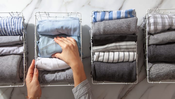 Person putting neatly folded clothes and pajamas in a metal mesh organizer basket on white marble table