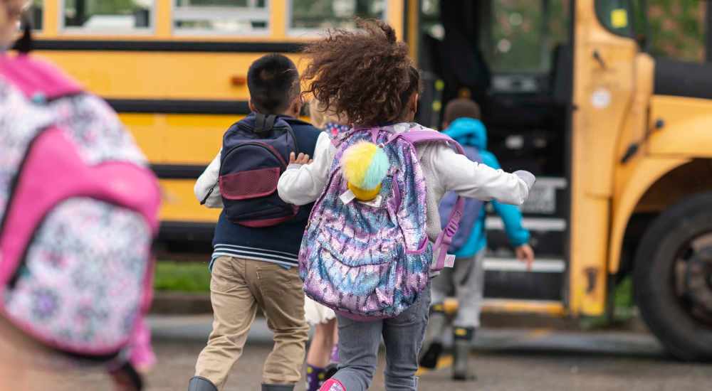 Children with backpacks running towards a school bus on a cloudy day at Carriages At Cedar Rock in Webster, New York