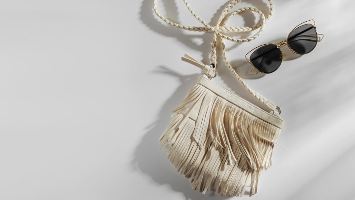 White fringe handbag with sunglasses on a plain white background. 