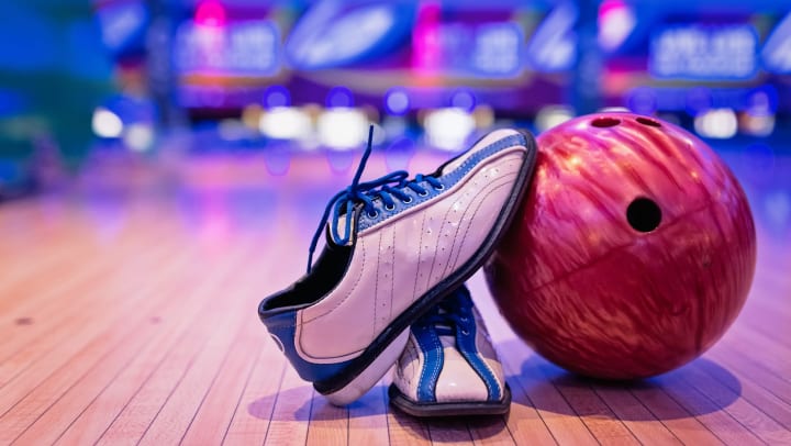 Bowling shoes sitting against bowling ball on the floor.