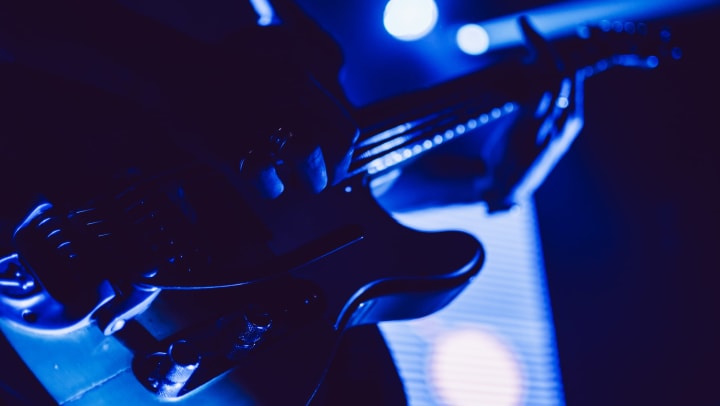 Person playing a guitar on stage with deep blue light shining in the background