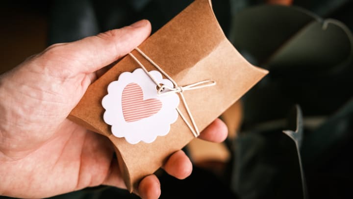 Hand holding a cardboard package wrapped in twine with a pink heart on it. 