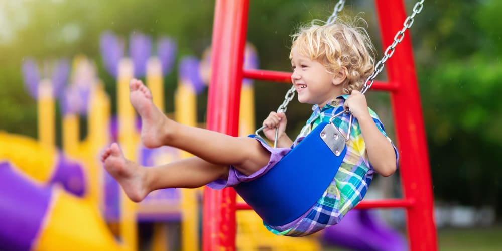 A young boy joyfully swings on a playground swing at Panorama at Arvada Ridge in Arvada, Colorado